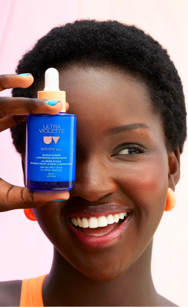 Woman holding a skincare product bottle with a dropper against a pink background